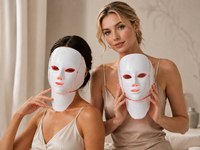 Two women with the Adreluma LED face and neck mask, one wearing it in red light mode and one holding it