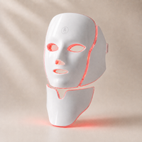 Adreluma LED face and neck mask lit in red light mode, three-quarter view with the touch button on the forehead